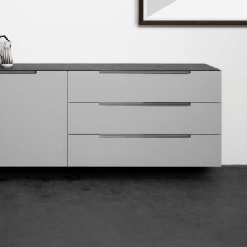 Modernes Interlübke-Sideboard mit drei horizontalen Schubladen und einer glatten schwarzen Arbeitsplatte vor einer weißen Wand, auf der ein Teil eines gerahmten Kunstwerks zu sehen ist.