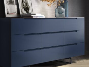 An der Wand steht eine moderne blaue Kommode von Mell, auf der Bücher, gerahmte Fotos und eine große Glasvase mit getrockneten Zweigen stehen - eine elegante Ergänzung, die vom Interlübke Sideboard-Design inspiriert ist.