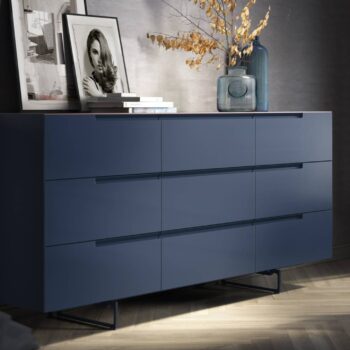 An der Wand steht eine moderne blaue Kommode von Mell, auf der Bücher, gerahmte Fotos und eine große Glasvase mit getrockneten Zweigen stehen - eine elegante Ergänzung, die vom Interlübke Sideboard-Design inspiriert ist.