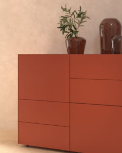 Ein roter Schrank mit klaren Linien steht vor einer beigen Wand, darauf eine Topfpflanze und zwei braune Ziervasen, daneben ein großer Spiegel.