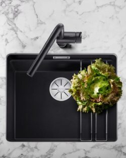 Draufsicht auf eine moderne schwarze Küchenspüle mit einem Salat, frischem Gemüse, Granatapfel und Gewürzzutaten auf einer Marmorarbeitsplatte.