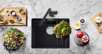 Draufsicht auf eine moderne schwarze Küchenspüle mit einem Salat, frischem Gemüse, Granatapfel und Gewürzzutaten auf einer Marmorarbeitsplatte.