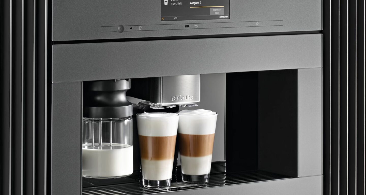 Eine eingebaute Kaffeemaschine schenkt zwei Lattes in Glastassen aus, auf der linken Seite ist ein Milchbehälter angebracht.