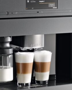 Eine eingebaute Kaffeemaschine schenkt zwei Lattes in Glastassen aus, auf der linken Seite ist ein Milchbehälter angebracht.
