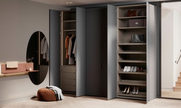 Ein moderner Kleiderschrank mit offenen Türen gibt den Blick frei auf Regale mit Schuhen, Taschen und Aufbewahrungsboxen, an die sich ein runder Spiegel, ein kleiner Tisch und ein Hocker anschließen - eine elegante Einrichtung, die vom Möbelhaus Bad Homburg inspiriert ist.