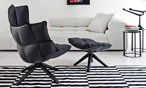 Ein modernes Wohnzimmer mit einem schwarzen, gepolsterten Sessel und einem dazu passenden Hocker, einem weißen Sofa, einem schwarzen Beistelltisch und einem schwarz-weiß gestreiften Teppich – alles zusammengestellt nach den Vorbildern des Möbelhauses Bad Homburg. Ein modernes Wohnzimmer mit einem schwarzen, gepolsterten Sessel und einem dazu passenden Hocker, einem weißen Sofa, einem schwarzen Beistelltisch und einem schwarz-weiß gestreiften Teppich – alles zusammengestellt nach den Vorbildern des Möbelhauses Bad Homburg.