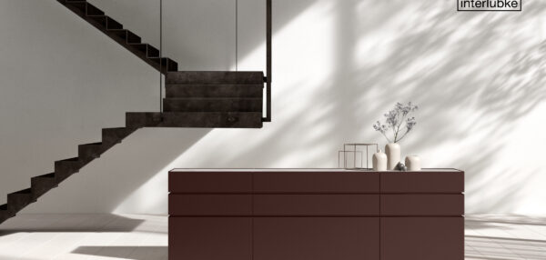 Modernes, minimalistisches Interieur von Braum Interior Design mit einer dunkelbraunen Kommode, dekorativen Vasen, geometrischen Dekorelementen, einer freitragenden Treppe und Schatten, die auf eine weiße Wand mit einem Interlübke-Logo in der oberen rechten Ecke fallen.