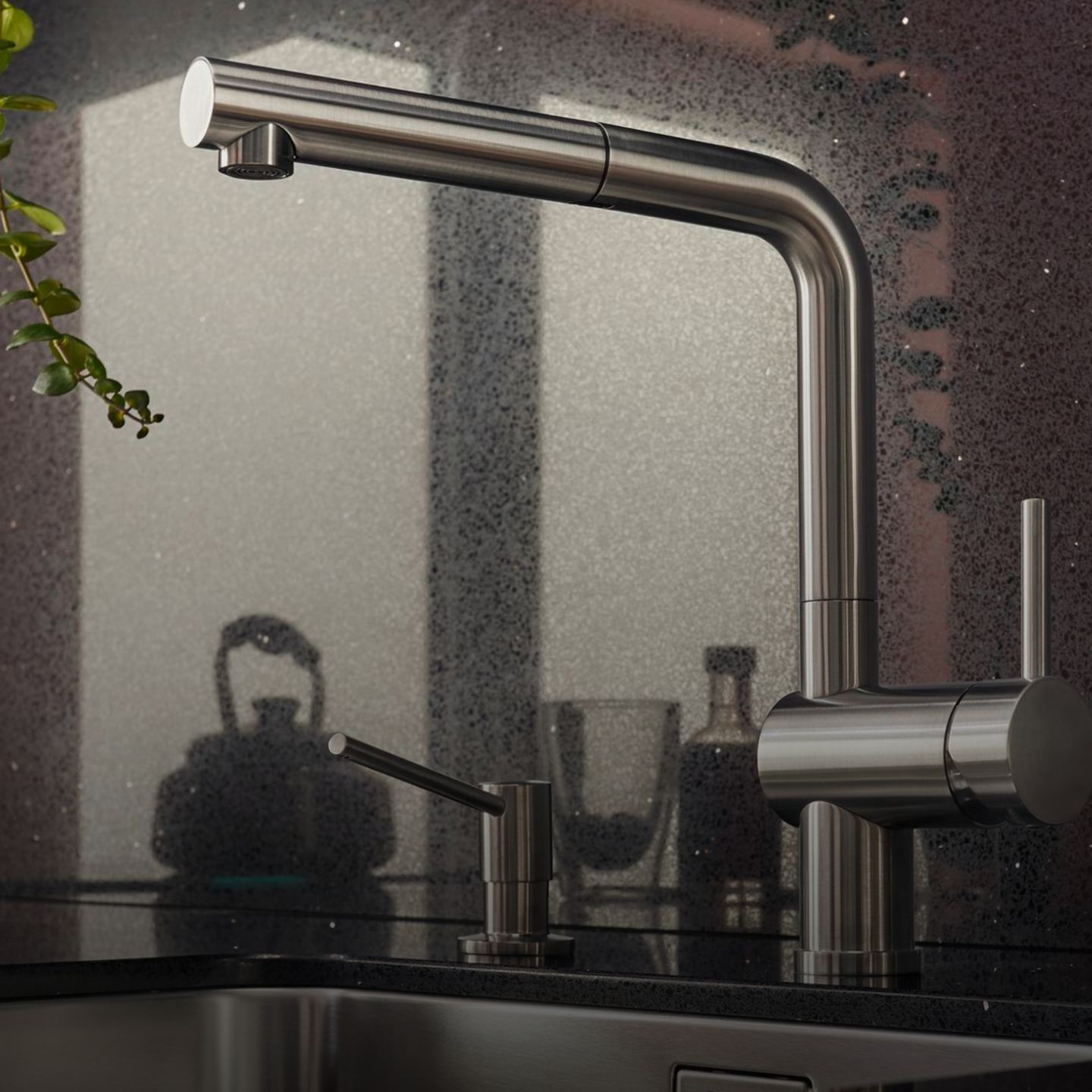 Eine moderne Blanco Linus Armatur aus rostfreiem Stahl mit seitlichem Griff und Seifenspender vor einer gesprenkelten Aufkantung mit verschiedenen, im Hintergrund verschwommenen Elementen.