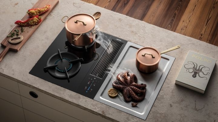 Ein modernes Bora-Kochfeld mit einem Topf auf einem Gasbrenner, ein weiterer Topf, ein Oktopus, der auf einer Grillplatte gegrillt wird, und ein Kochbuch mit dem Titel Polpo auf dem Tresen.