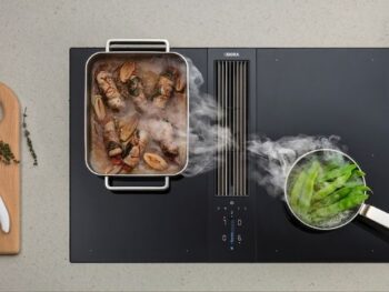 Draufsicht auf ein Bora-Induktionskochfeld mit einem Topf mit gekochtem Fleisch und Gemüse auf der linken Seite und kochendem grünem Gemüse auf der rechten Seite; der Dampf wird durch einen Abzug abgeleitet.