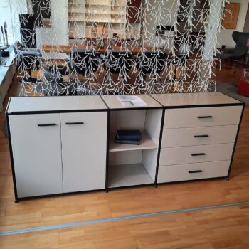 Ein Dauphin Home Sideboard mit zwei Schränken, vier Schubladen und offenen Regalen steht auf einem Holzfußboden, ergänzt durch einen dekorativen weißen Hängetrenner im Hintergrund.