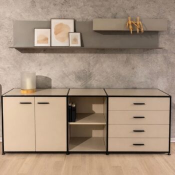 Modernes Sideboard von Dauphin Home mit Regalen und Schubladen, minimalistisches Dekor mit gerahmter Kunst, zwei Holzfiguren auf einem Wandregal und einer Lampe auf einem hellen Holzboden vor einer grau strukturierten Wand.
