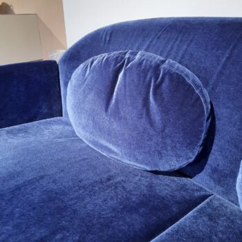 Blaues Samtsofa mit einem ovalen, passenden Kissen an der Rückenlehne, abgebildet in einem gut beleuchteten Innenraum.