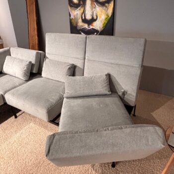 Ein modernes, hellgraues Brühl-Sofamodul mit verstellbarer Rückenlehne und Armlehnen steht auf einem beigen Teppich, hinter dem ein farbenfrohes, abstraktes Porträt an der Wand hängt. Dieses „Roro Soft“-Design verleiht Ihrem Wohnbereich sowohl Komfort als auch zeitgemäßen Stil.