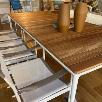 Rechteckiger Esstisch aus Teakholz mit weißem Gestell, umgeben von weißen Netzstühlen; drei braune Vasen stehen auf einem Tablett auf dem Tisch in einem gut beleuchteten Innenbereich, der an den stilvollen Mirto Outdoortisch von B&B Italia erinnert.