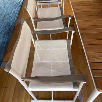 Zwei weiße Mirto Outdoor Netzstühle von B&B Italia mit grauen Armlehnen stehen neben einem Holztisch auf einem Holzboden.