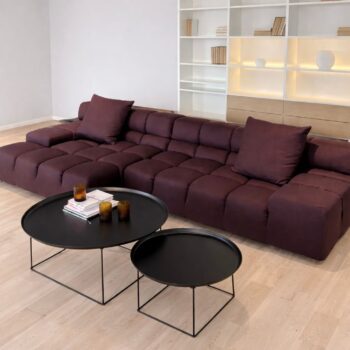 Ein modernes Wohnzimmer mit einem niedrigen kastanienbraunen Tufty-Time-Sofa von B&B Italia, zwei runden schwarzen Couchtischen mit Büchern und Glastassen und eingebauten Regalen im Hintergrund.