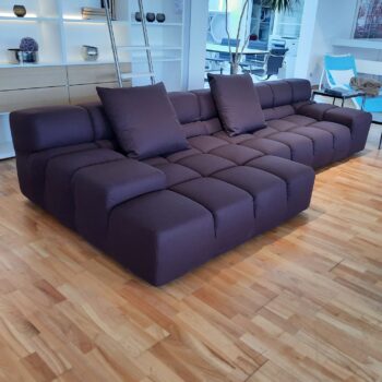 Großes, modernes, dunkelviolettes Tufty-Time-Sofa mit getuftetem Design und vier Kissen auf einem hellen Holzboden in einem zeitgenössischen Wohnbereich mit Regalen und Dekoration - ein ikonisches Designersofa von B&B Italia.