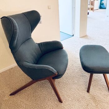 Ein moderner dunkelgrauer Cassina Sessel mit Holzbeinen steht zusammen mit einem passenden Cassina Hocker auf einem hellen Teppichboden im Raum.