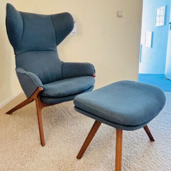 Ein moderner blauer Cassina Sessel mit hoher Rückenlehne und ein passender Cassina Hocker, beide mit Holzbeinen, stehen auf einem beigen Teppich in einem hellen Raum.