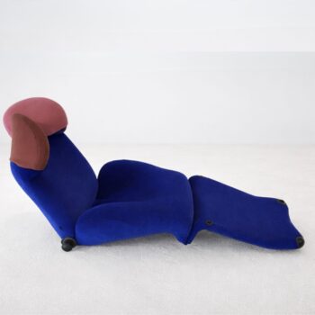 Ein moderner Klassiker-Sessel von Cassina mit blauer Polsterung, rosa und brauner Kopfstütze und verlängerter Fußstütze steht auf einem hellen Boden - ein echtes Wink-Design-Statement.