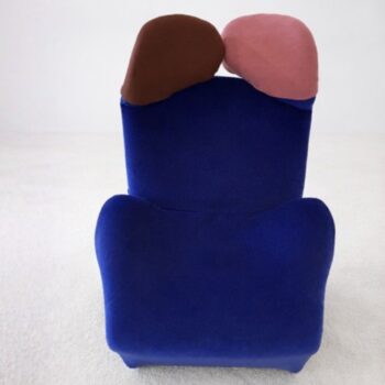 Ein blauer Cassina Wink Sessel mit zwei Kissen, einem braunen und einem rosafarbenen, die an stilisierte Köpfe erinnern.