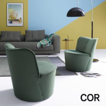 Zwei grüne Nenou-Sessel in einem Raum mit einem grauen Sofa, einer Stehlampe und einem Teppich vor einer blau-gelben Wand.