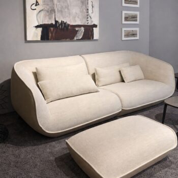 Ein modernes COR NOOK Sofa mit passenden Kissen und Ottomane steht auf einem grauen Teppich in einem Raum, der mit abstrakter Wandkunst und gerahmten Bildern geschmückt ist.