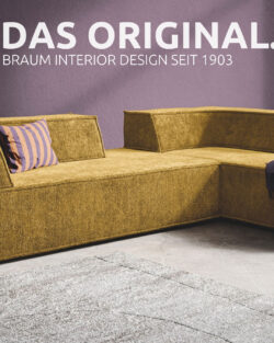 Modernes, senfgelbes Ecksofa mit violetten Zierkissen in einem zeitgenössischen Wohnzimmer mit violetten Wänden. An der Wand steht in weißer Schrift: „DAS ORIGINAL“. Erleben Sie zeitlosen Stil mit Braum Interior Design – SEIT 1903.