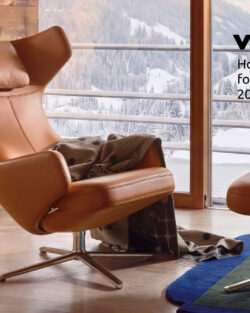 Ein Ledersessel mit einer Decke, einem passenden Hocker und einem Beistelltisch steht vor einem Fenster mit Blick auf schneebedeckte Berge. Diese einladende Einrichtung, die gutes Design verkörpert, ist Teil der Kollektion „Vitra Home Stories for Winter 2026/2027“. Ein Schriftzug mit der Aufschrift „Homestories für den Winter 2026/2027“ rundet das Bild ab.