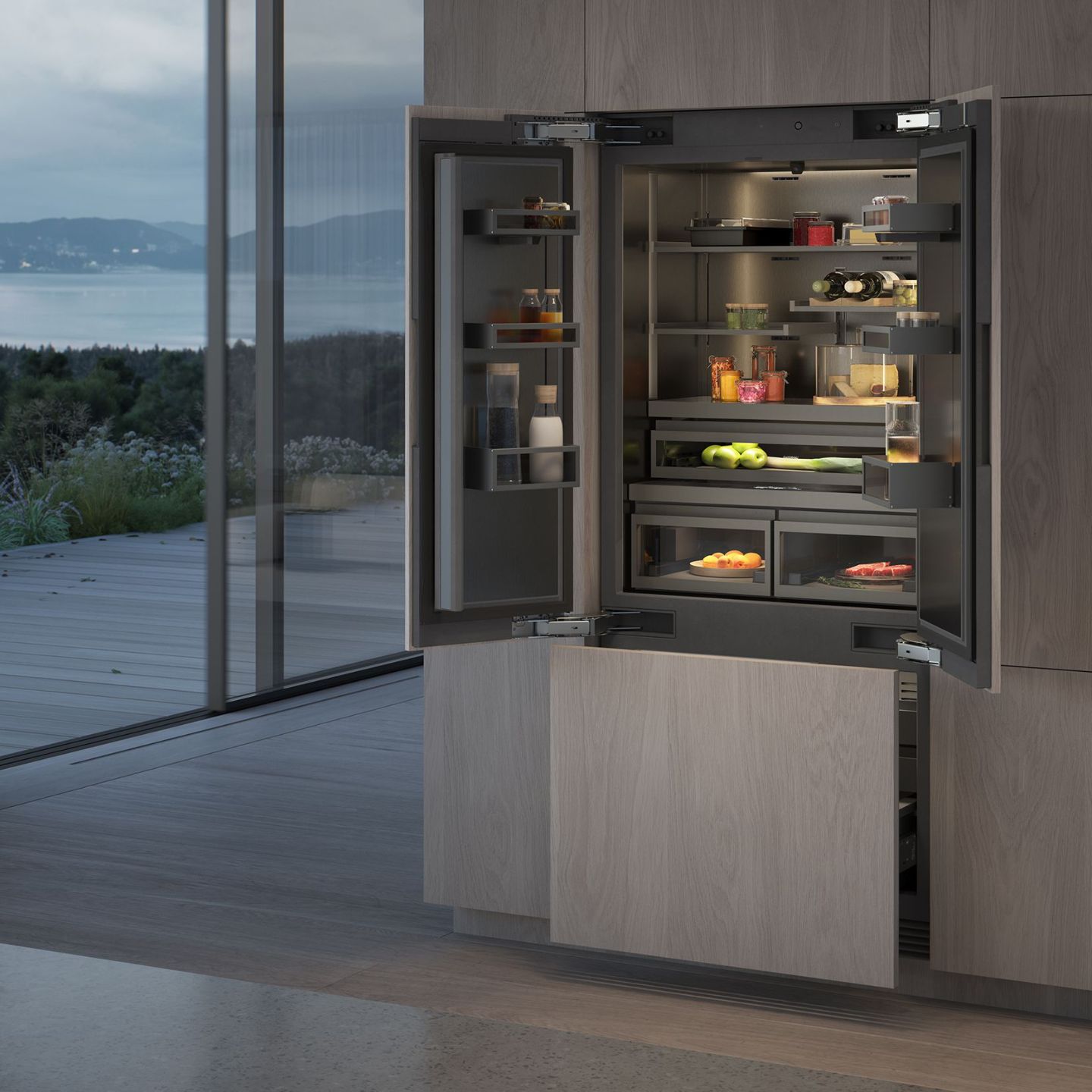 Ein moderner Einbaukühlschrank der Serie 400 von Gaggenau mit offenen Türen präsentiert ordentlich geordnete Lebensmittel und Getränke in einer Küche mit großen Fenstern und Blick auf einen malerischen Außenbereich.