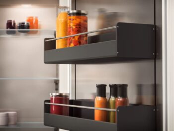 Gaggenau 400 Vario Serie: Zwei Ablagen in der Tür eines Gaggenau 400 Kühlschranks nehmen Flaschen und Gläser mit verschiedenen Flüssigkeiten und Konserven auf. Im Hintergrund sieht man das Innere des Kühlschranks, der zur 400 Vario Serie gehört, mit weiteren Gläsern.