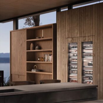 Gaggenau 400 Vario Serie: Moderne Küche mit Holzvertäfelung, offenen Regalen mit Dekoration und Büchern sowie einem zweitürigen Glaskühlschrank der Serie 400 von Gaggenau, der mit Weinflaschen bestückt ist.
