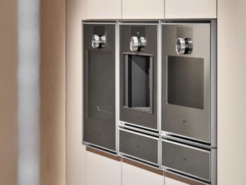 Gaggenau Expressive: In einer modernen, hellen Schrankwand sind drei Gaggenau Edelstahl-Einbaugeräte mit Digitalanzeige und Bedienknöpfen aus der Expressive Serie nebeneinander eingebaut.