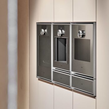 Gaggenau Expressive: In einer modernen, hellen Schrankwand sind drei Gaggenau Edelstahl-Einbaugeräte mit Digitalanzeige und Bedienknöpfen aus der Expressive Serie nebeneinander eingebaut.