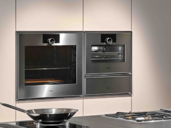 Gaggenau Expressive: Eine moderne Küche mit Gaggenau Edelstahl-Einbaubacköfen, einem Gas-Kochfeld und einer Bratpfanne auf der Theke im Vordergrund aus der Expressive Serie.