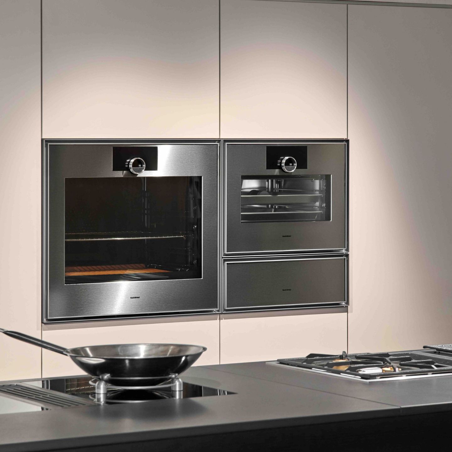 Eine moderne Küche mit Gaggenau Edelstahl-Einbaubacköfen, einem Gas-Kochfeld und einer Bratpfanne auf der Theke im Vordergrund aus der Expressive Serie.