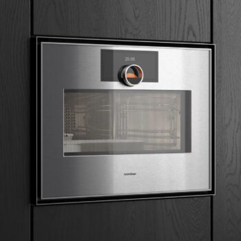 Gaggenau Expressive: Eine Einbau-Mikrowelle aus Edelstahl von Gaggenau aus der Expressive Serie mit digitaler Timer-Anzeige und Bedienknopf in einem dunklen Holzschrank.