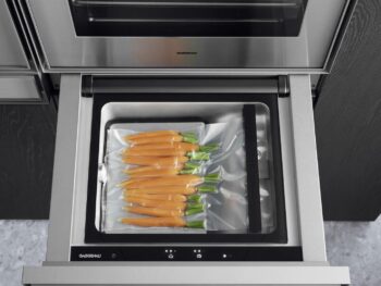 Gaggenau Expressive: Ein Vakuumiergerät der Gaggenau Expressive Serie mit vakuumversiegelten frischen Karotten in einem Plastikbeutel unter einem Einbauofen in einer modernen Küche.
