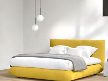 Ein modernes Schlafzimmer mit einem niedrigen gelben Interlübke-Bett, weißer Bettwäsche, einer grauen Decke, zwei Kugel-Pendelleuchten und Sonnenlicht, das auf die weißen Wände und den Holzboden fällt.