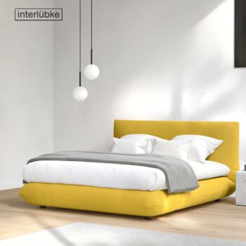 Ein modernes Schlafzimmer mit einem niedrigen gelben Interlübke-Bett, weißer Bettwäsche, einer grauen Decke, zwei Kugel-Pendelleuchten und Sonnenlicht, das auf die weißen Wände und den Holzboden fällt.