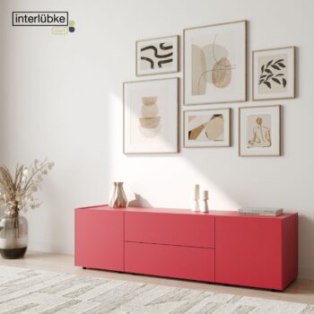 Rotes Interlübke Sideboard vor einer weißen Wand, links eine Vase mit getrockneten Pflanzen, darüber sechs abstrakte Bilderrahmen. Das Sonnenlicht wirft sanfte Schatten auf diese moderne Szene.