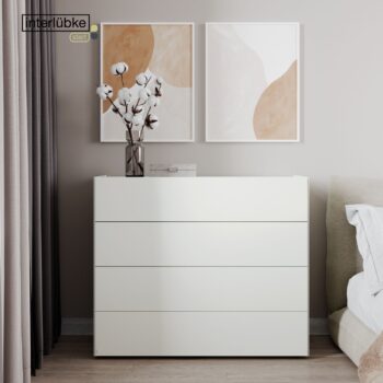 Eine weiße Interlübke-Kommode mit vier Schubladen steht vor einer beigen Wand, auf der eine Vase mit Baumwollstängeln steht, darunter zwei abstrakte Kunstdrucke - der perfekte Anfang für ein elegantes Sideboard.