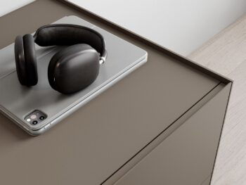 Ein Paar Over-Ear-Kopfhörer und ein Smartphone ruhen auf einem geschlossenen Laptop, der auf einem mattbraunen Sideboard steht. Das Interlübke-Logo erscheint in der oberen rechten Ecke und sorgt für einen perfekten Start in den Tag.