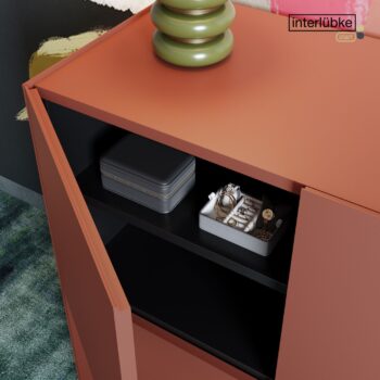 Ein orangefarbenes Interlübke-Sideboard mit offenen Türen gibt den Blick frei auf ein graues Kästchen und ein Tablett mit Schmuck und einer Uhr in einem schwarzen Regal.