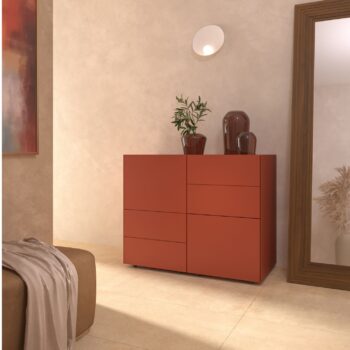 Ein modernes Zimmer mit einem Interlübke-Sideboard in Rot mit dekorativen Vasen und einer Pflanze, einem großen Spiegel mit Holzrahmen, beigen Wänden und einer stilvollen Würfelleuchte für die Wandmontage.