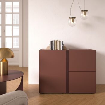 Minimalistisches Zimmer mit lilafarbenem Interlübke-Sideboard mit Büchern und Dekoration, rundem Tisch mit Messinglampe, Holzboden und hängenden Cube light-Glaspendelleuchten.