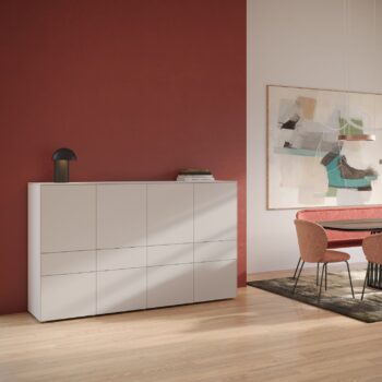 Ein modernes Esszimmer mit einem Interlübke Sideboard, einer Cube-Leuchte auf dem schwarzen Tisch, einer roten Akzentwand, abstrakten Kunstwerken und einem Esstisch mit roten Stühlen auf einem dunklen Teppich.