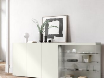 Minimalistisches Interlübke-Sideboard mit geschlossenen Schränken auf der linken Seite und Glasböden auf der rechten Seite für Bücher und Keramik; eine Vase, gerahmte Kunst und eine elegante Würfelleuchte sind darauf ausgestellt.