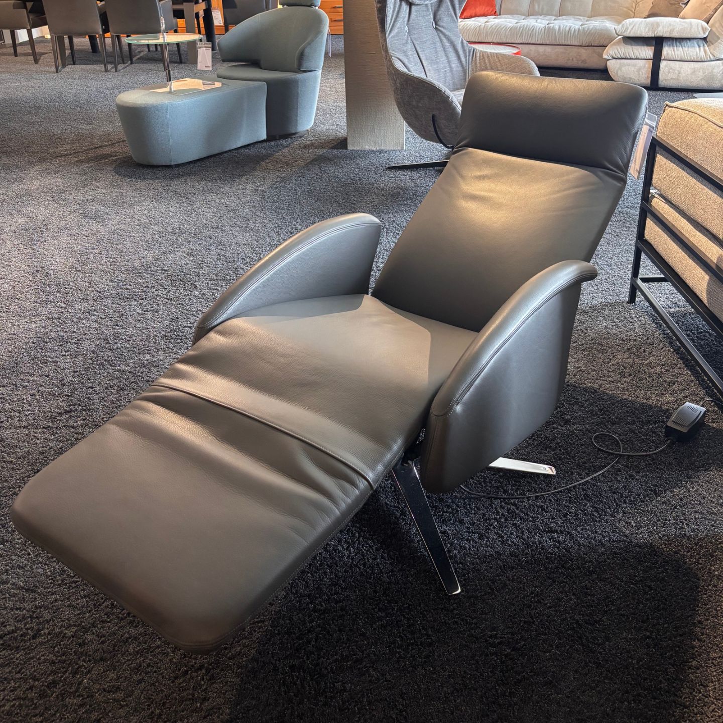 Ein IP Design-Funktionssessel, der „Cliff“ – ein Liegesessel aus schwarzem Leder mit verlängerter Fußstütze –, steht auf einem dunklen Teppichboden in einem Möbelausstellungsraum. Ein IP Design-Funktionssessel, der „Cliff“ – ein Liegesessel aus schwarzem Leder mit verlängerter Fußstütze –, steht auf einem dunklen Teppichboden in einem Möbelausstellungsraum.